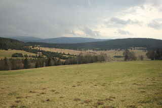 Pohled na býv. Zhůří z úbočí Hadího vrchu (1021 m n.m.), vzadu hraniční hory Debrník (1336 m n.m.), Polom ( 1295 m n.m.)